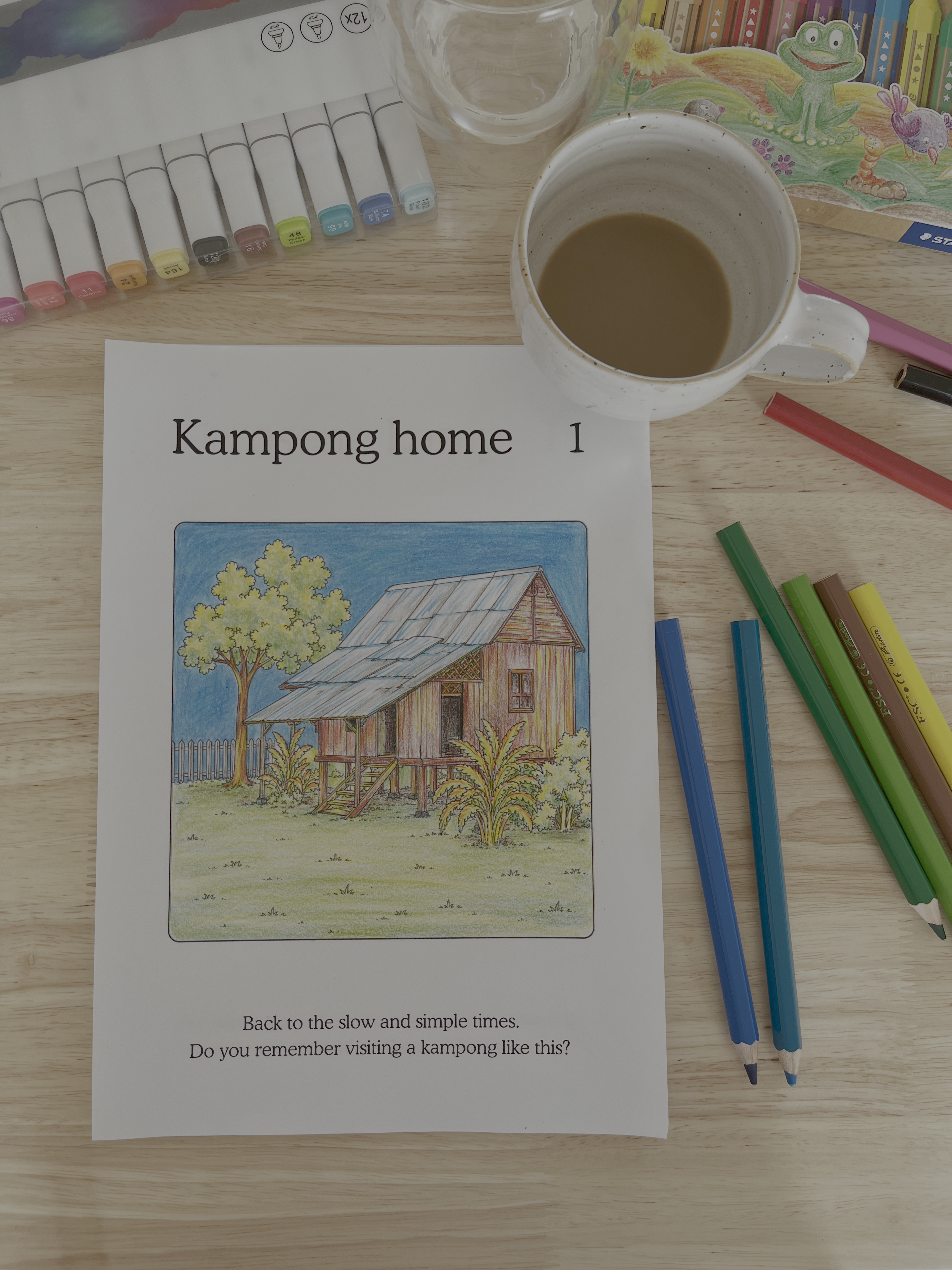 Coloring page with a kampong illustration on a table with coloring supplies